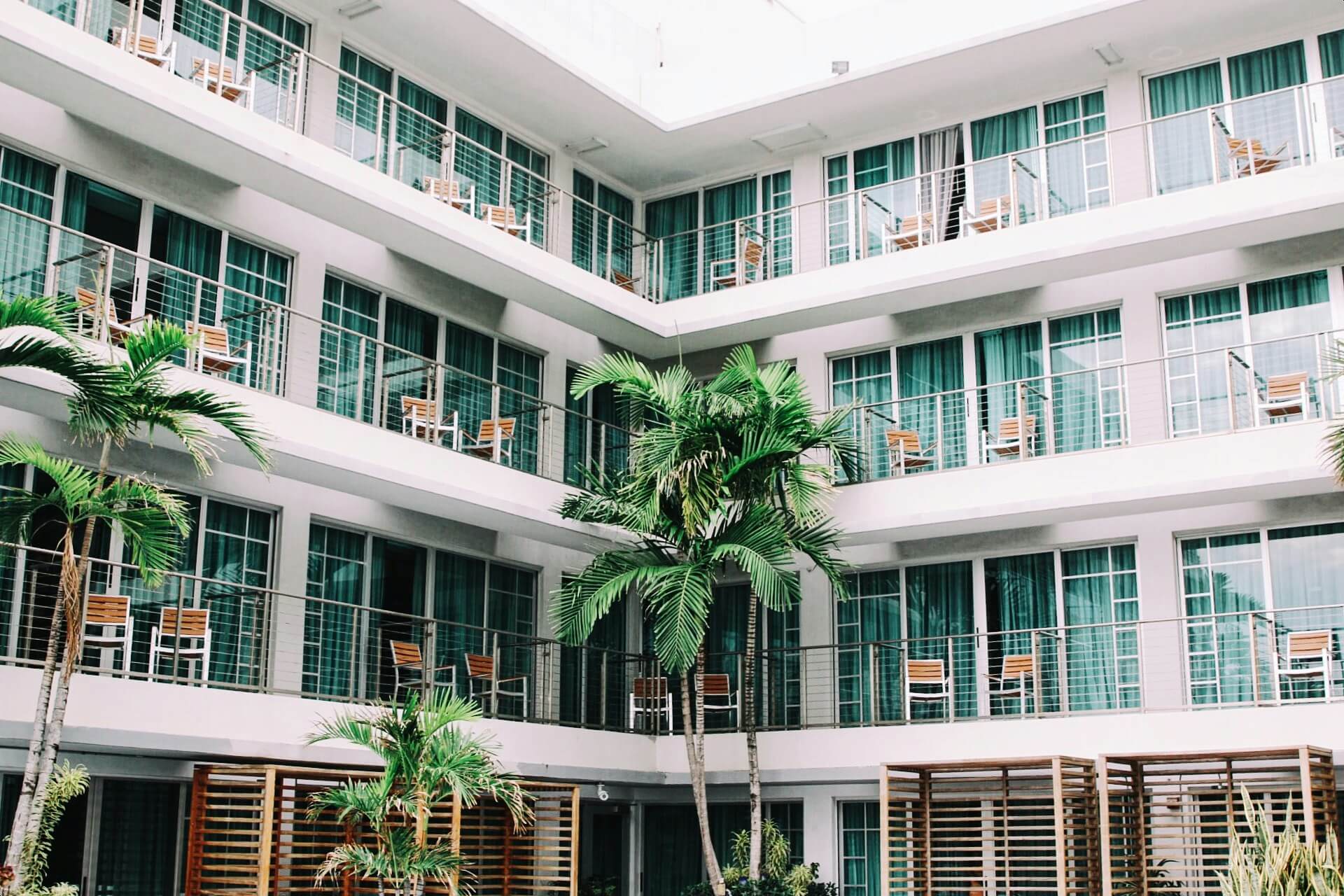 Hôtel avec des chaises sur les balcons et des palmiers dans la cour